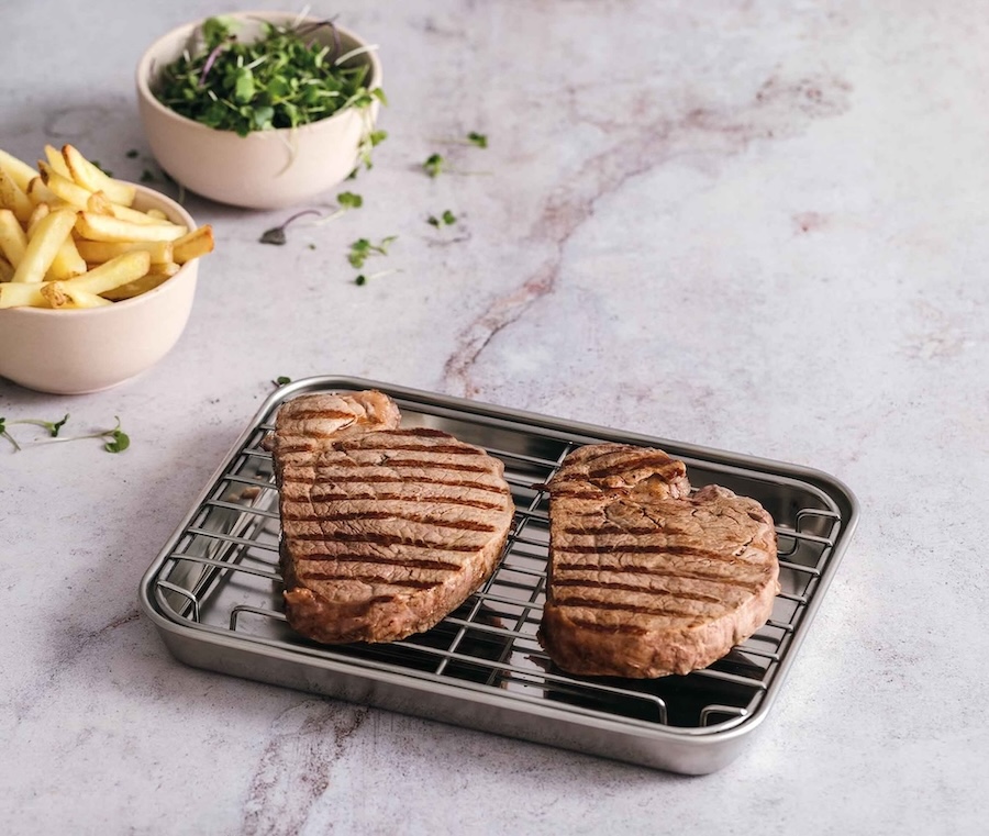 Paistopelti ritilällä jonka päällä kaksi grillattua pihviä